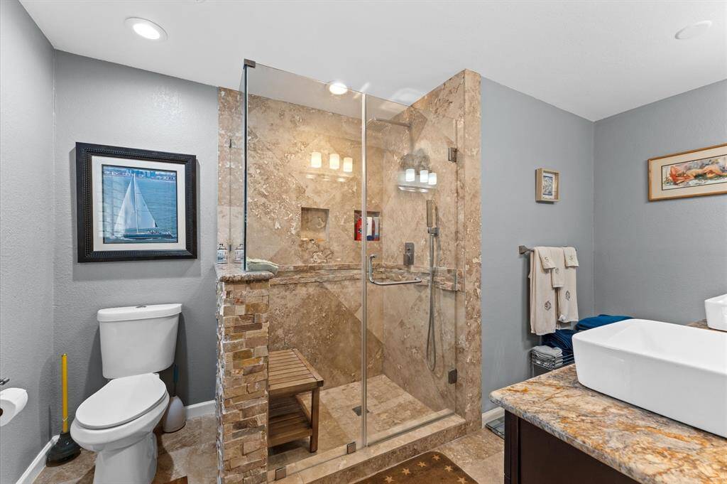 Primary bath features elegant stone tile walls and spacious glass-enclosed walk-in shower