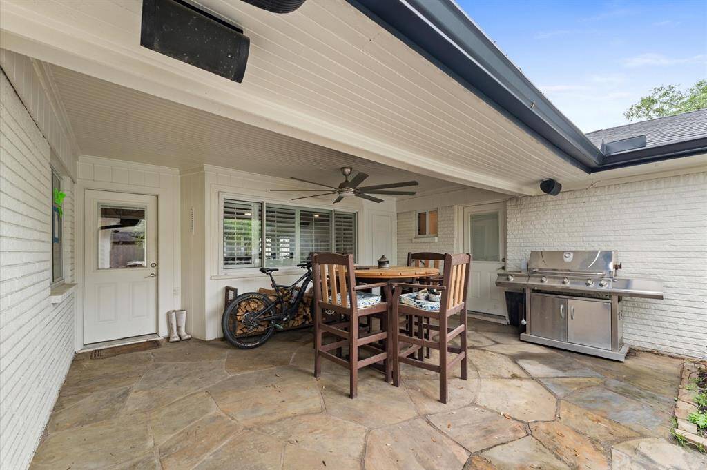 Cozy covered patio with a ceiling fan, perfect for outdoor dining. It features a stone floor, a high table with chairs, and a built-in grill, creating an inviting space for entertaining.