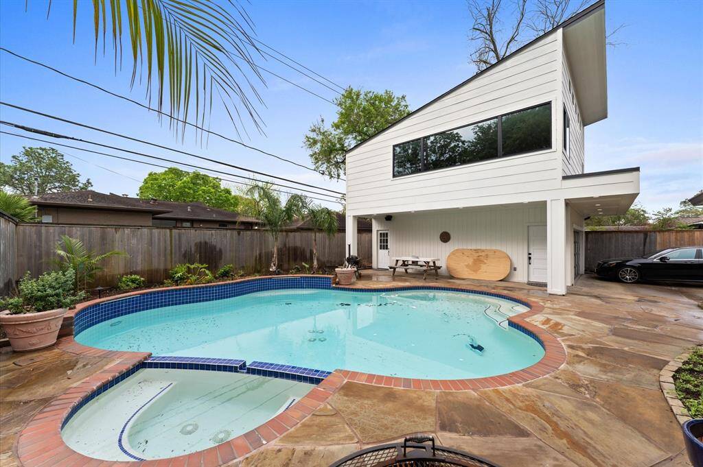 This photo showcases a modern backyard with a unique angular two-story structure. It features a swimming pool and hot tub surrounded by a stone patio, complemented by potted plants and a wooden privacy fence. Ideal for relaxation and outdoor entertaining.