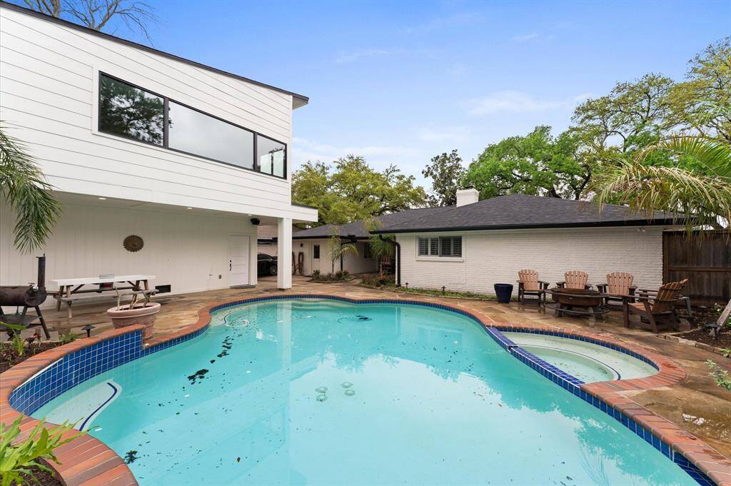 This backyard features a spacious pool with adjacent seating areas, surrounded by lush landscaping. The jewel home has a covered patio, offering a perfect space for relaxation and entertaining.