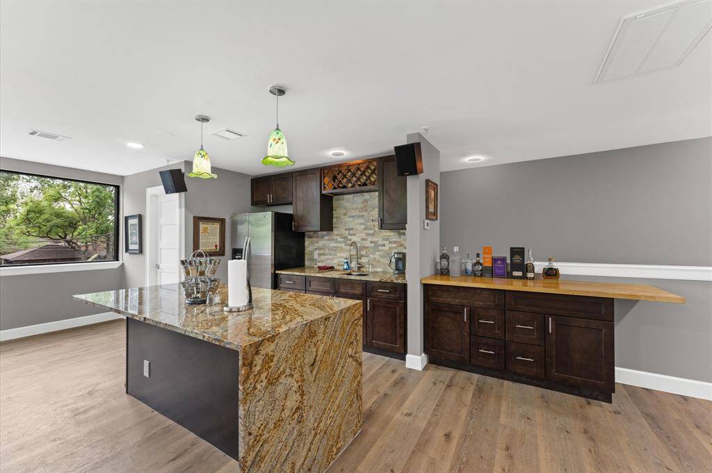 This modern kitchen features a sleek design with dark wood cabinets, a granite island, and a stylish backsplash. It includes ample natural light, stainless steel appliances, and a wine rack, offering a perfect blend of functionality and elegance.