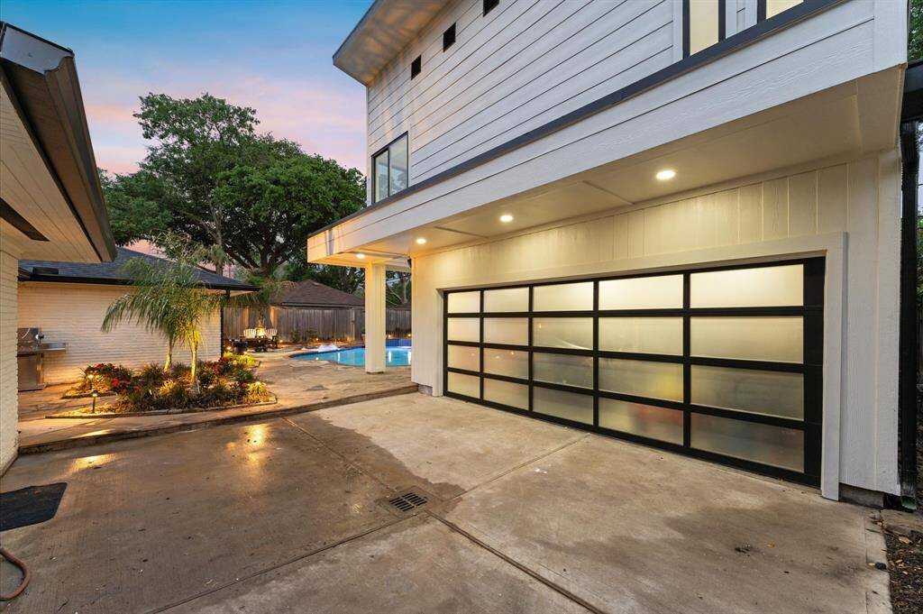 Sleek frosted glass garage door, spacious driveway, and well-lit exterior. Features a landscaped backyard with a pool and patio area, perfect for outdoor entertaining.