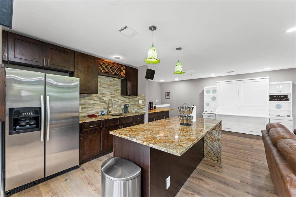 Open concept garage apartment with fully equipped kitchen and breakfast bar. Gorgeous kitchen features dark wood cabinetry, a stainless steel refrigerator, and a spacious granite island with pendant lighting.