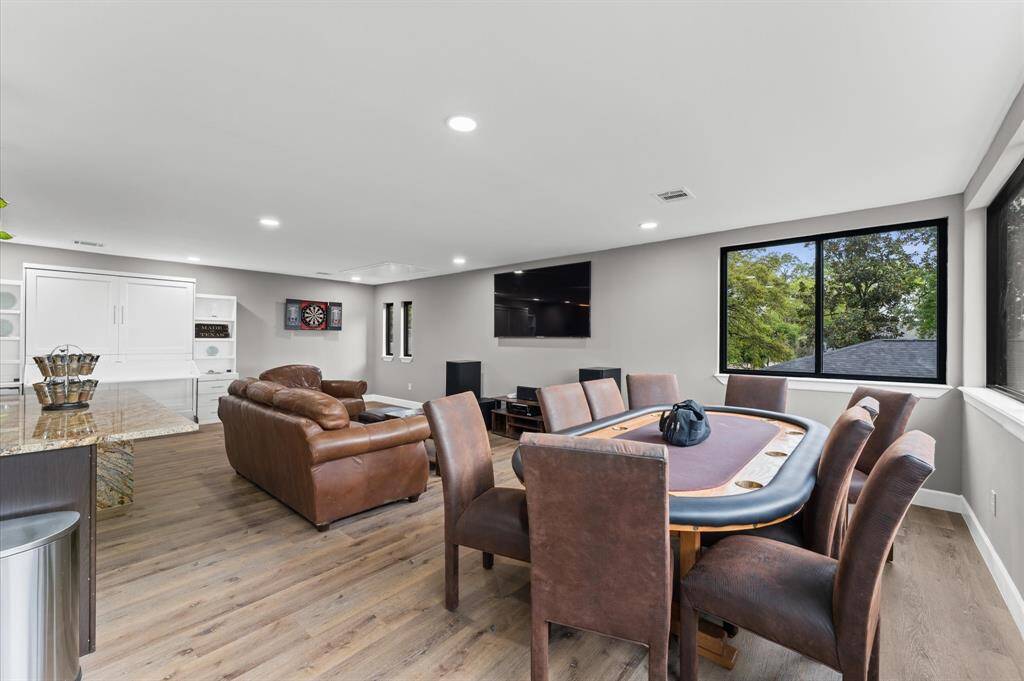 Ample entertainment room with large windows, featuring a poker table, leather seating, dartboard, and mounted TV. Bright and inviting with modern décor and ample natural light.