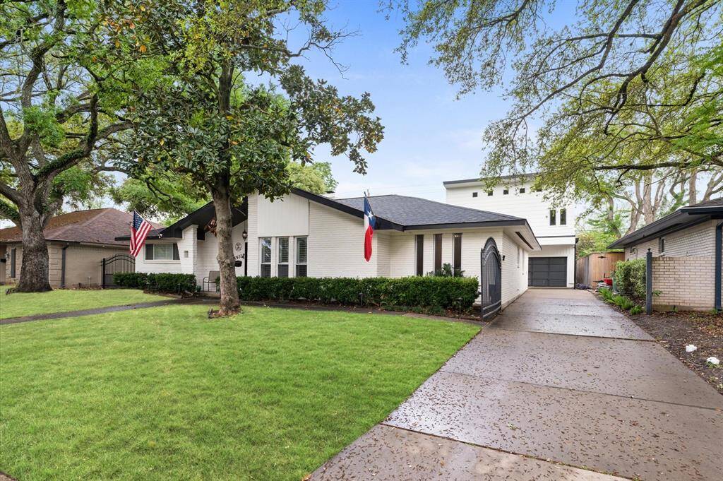 Lovely single-story home with a clean white exterior, nestled among mature trees. Features a manicured lawn, a long driveway, and a welcoming front entrance.