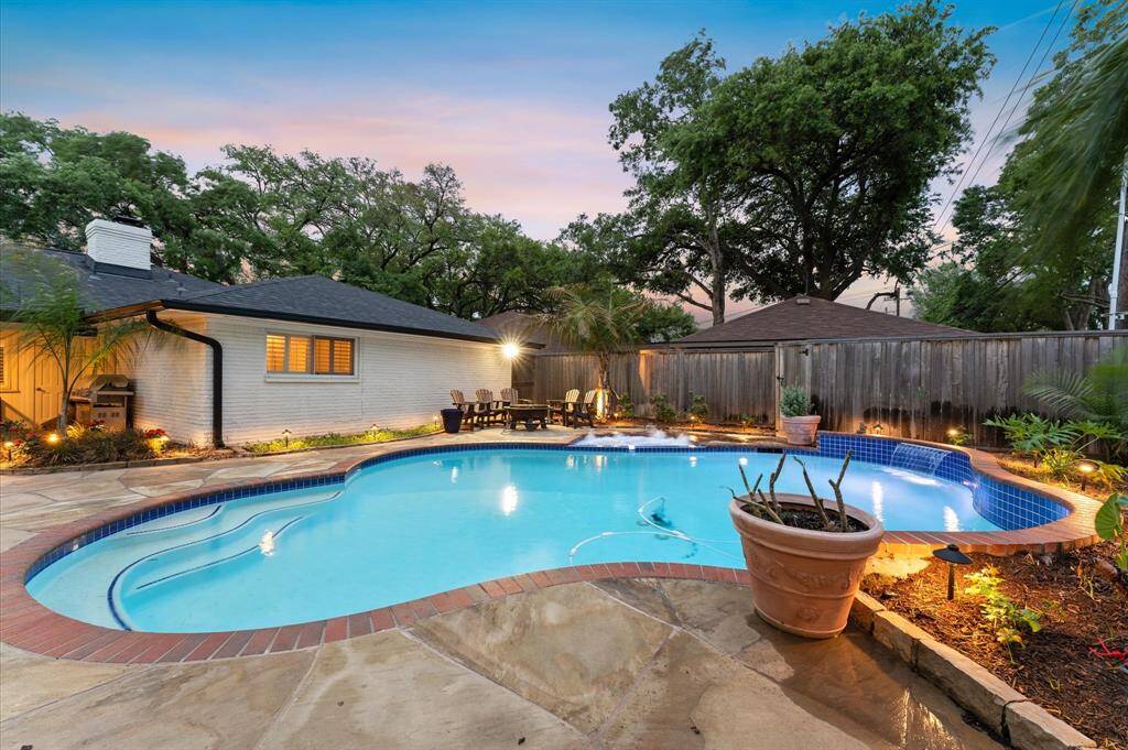 This photo showcases a modern backyard with a unique angular two-story structure. It features a swimming pool and hot tub surrounded by a stone patio, complemented by potted plants and a wooden privacy fence. Ideal for relaxation and outdoor entertaining.