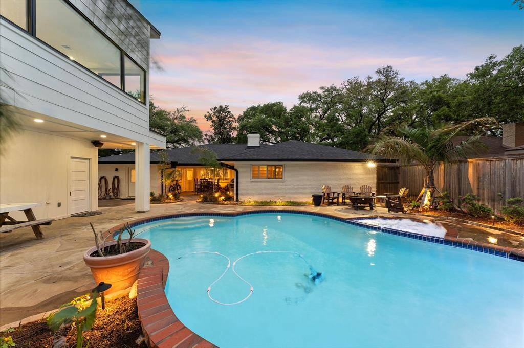 This inviting backyard features a well-lit swimming pool with a curved design, surrounded by landscaped gardens and a cozy seating area perfect for outdoor gatherings.