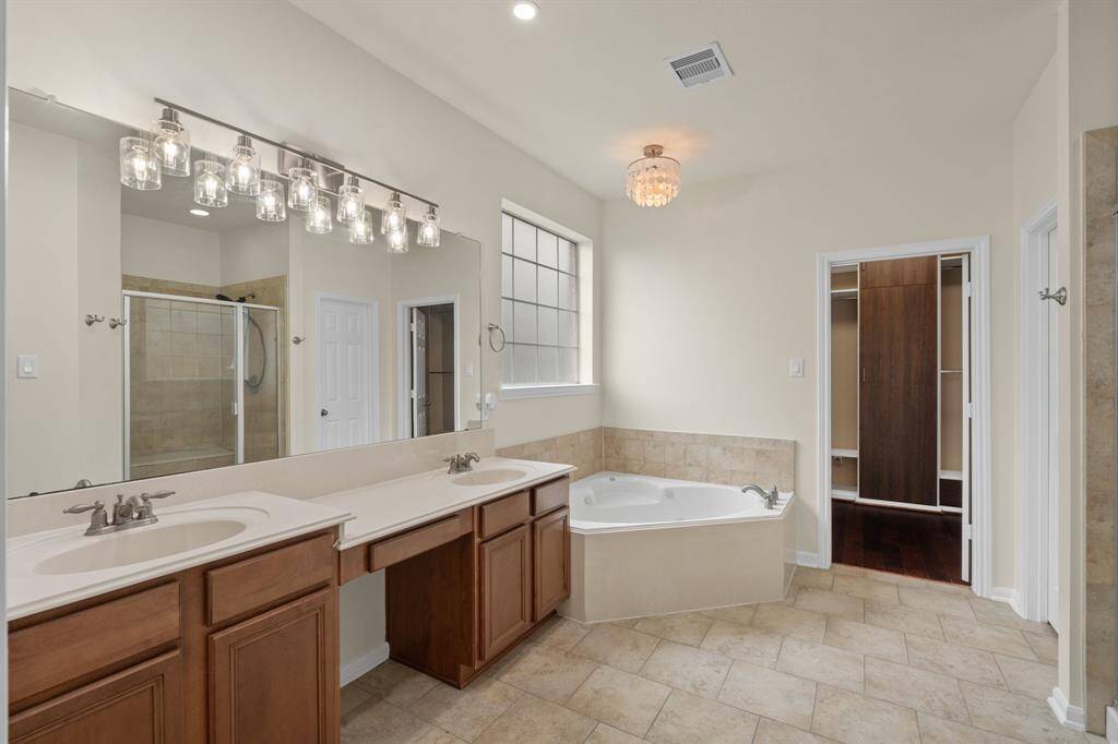 This spacious primary bathroom is a true retreat, featuring a relaxing jetted tub, convenient double sinks, a separate standing shower, and direct access to an incredibly spacious and upgraded closet.