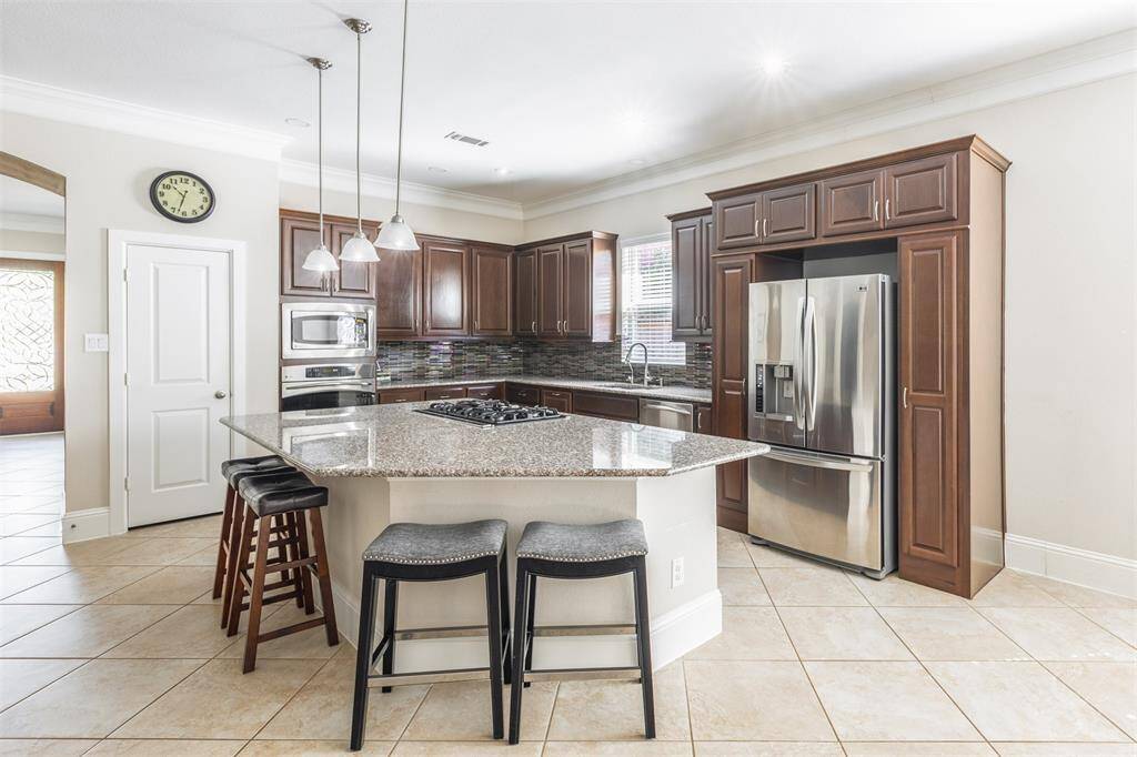 The spacious kitchen boasts rich cabinetry, gorgeous granite countertops, and a huge granite topped island with a gas cooktop and bar seating under pendant lighting. Stainless steel appliances and a designer tile backsplash complete this polished culinary space.