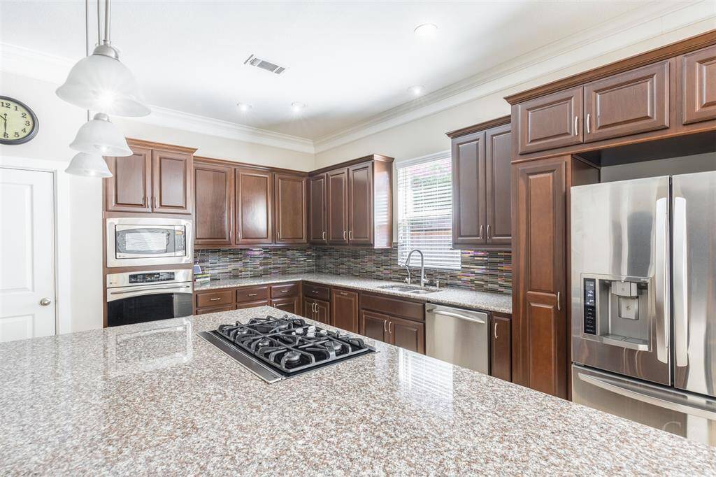 A gleaming granite island anchors the kitchen, featuring a built-in gas cooktop and pendant lighting. With ample cabinetry and counter space, this kitchen balances function with upscale design.