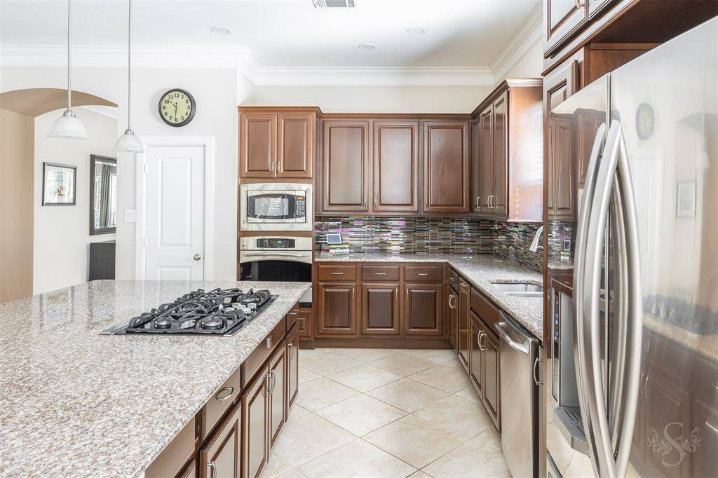 This elegant gourmet kitchen reveals a large convenient island with gorgeous granite countertop, gas cooktop, stainless steel appliances and rich cabinetry that creates an inviting cooking environment.