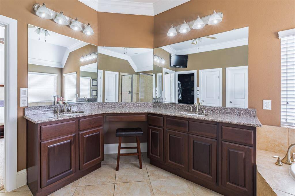 An extended vanity with granite countertop, double sinks and a built-in makeup space provide both style and convenience. Framed by a wall mirror and under soft lighting, the space is perfectly appointed for daily routines.