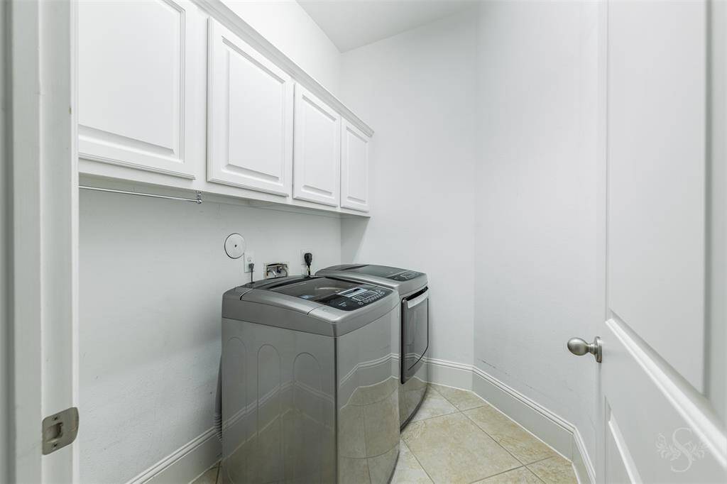 The laundry room features upper cabinetry for convenient storage and ample room for full-size appliances. Neutral tile floors and crisp white finishes create a bright, functional space.