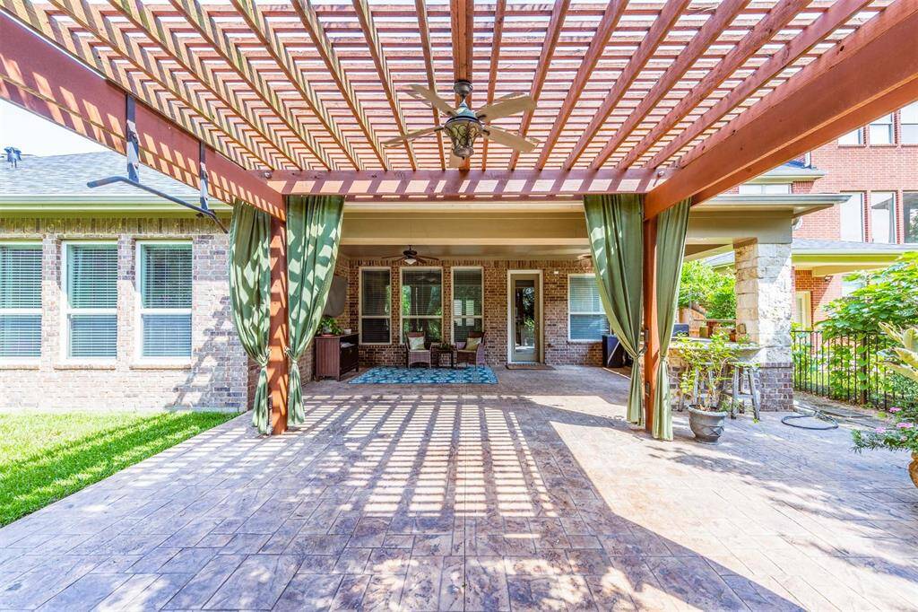 This expansive stamped concrete patio is framed by a stunning pergola with draped curtains and a ceiling fan, creating an inviting outdoor retreat. The seamless flow to the covered back porch offers a stylish and shaded setting for relaxing or entertaining.