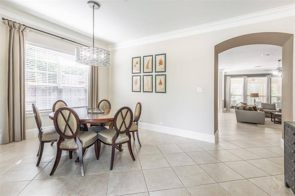 Enjoy meals in this spacious dining area featuring oversized tile floors, a statement light fixture, and a large window with blinds. An arched entry to the family room adds character and flow to the layout.