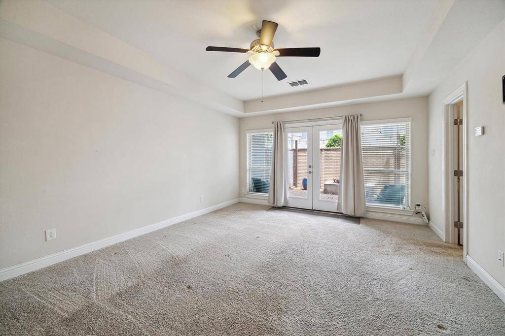 Secondary bedroom located on first level features neutral walls, plush carpeting, and a ceiling fan. Large windows and glass doors offer plenty of natural light and lead to an outdoor space.