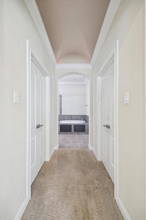 Hallway from primary bedroom with carpeted flooring leading to a bathroom featuring a bathtub and tiled floor. The hallway has two walkin closets on either side, and the ceiling is vaulted.