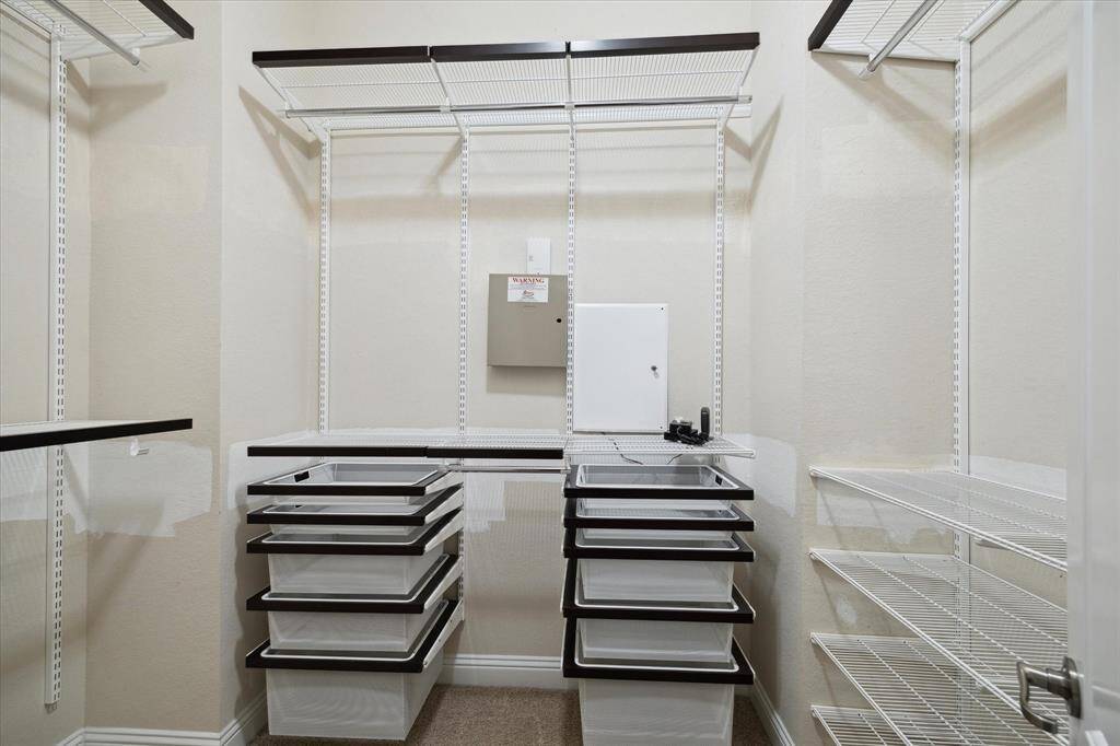 This is a well-organized walk-in closet with multiple wire shelves and pull-out drawers, offering ample storage space. The neutral color scheme and efficient layout make it functional and easy to personalize.