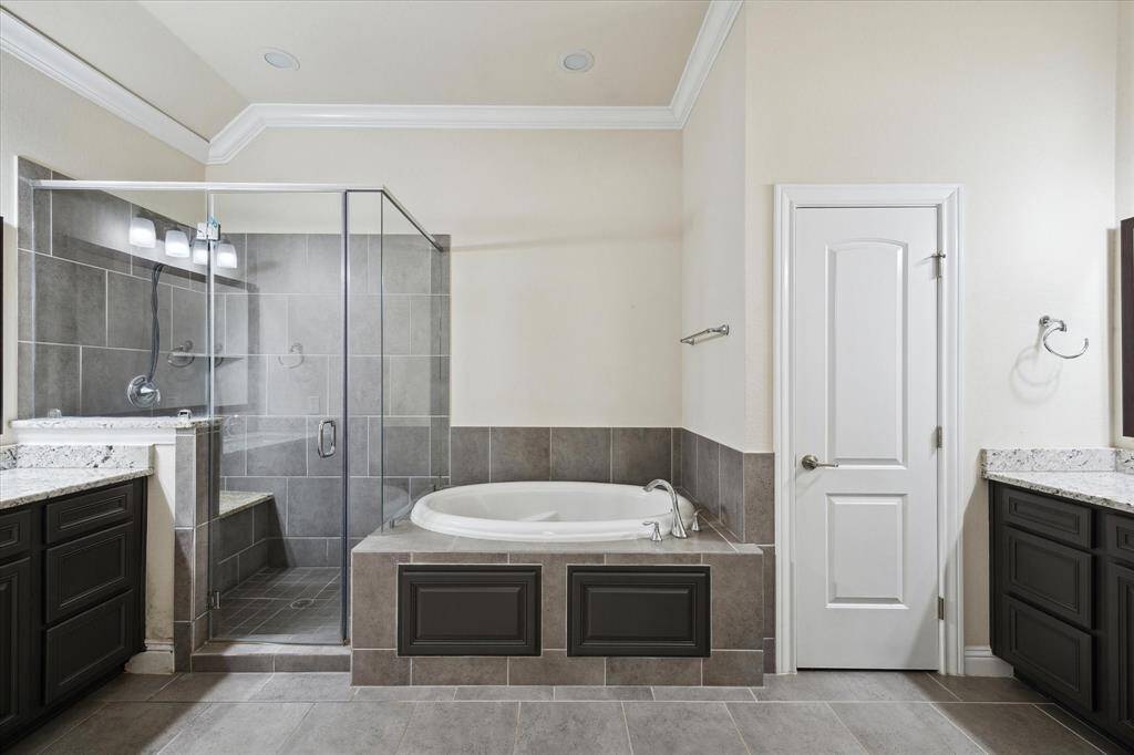 Primary bathroom showcases a modern bathroom featuring a spacious glass-enclosed shower, a large soaking tub, and dual vanities with granite countertops, offering a luxurious and functional space.
