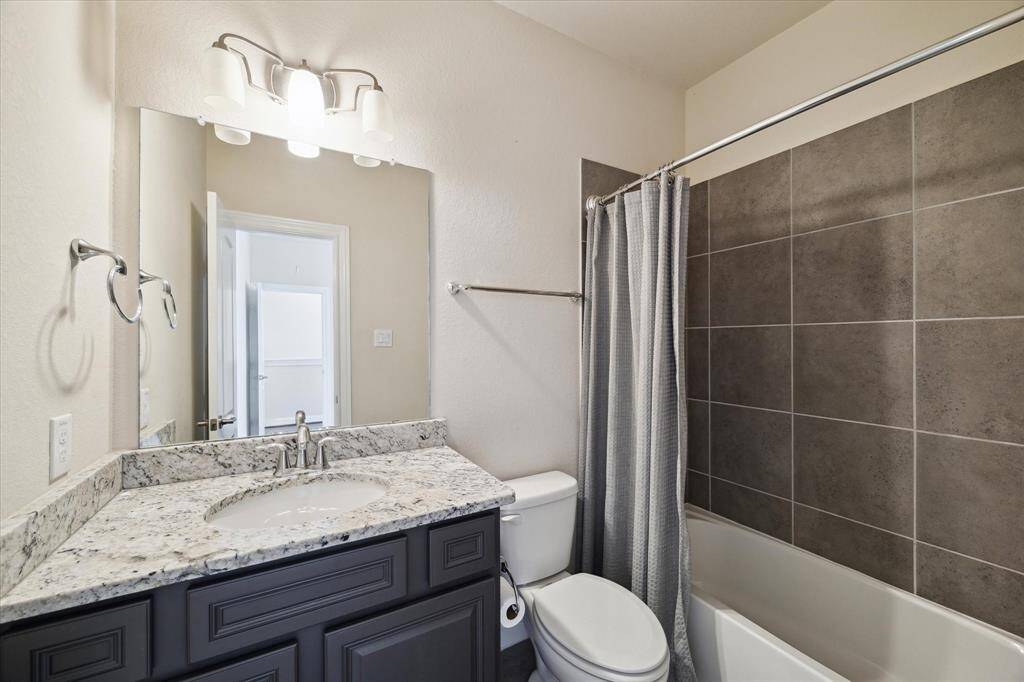 The bathroom features a modern design with a granite countertop, under-mount sink, and dark cabinetry. It includes a tiled shower and tub combination with a sleek curtain, and a large mirror with elegant lighting above.