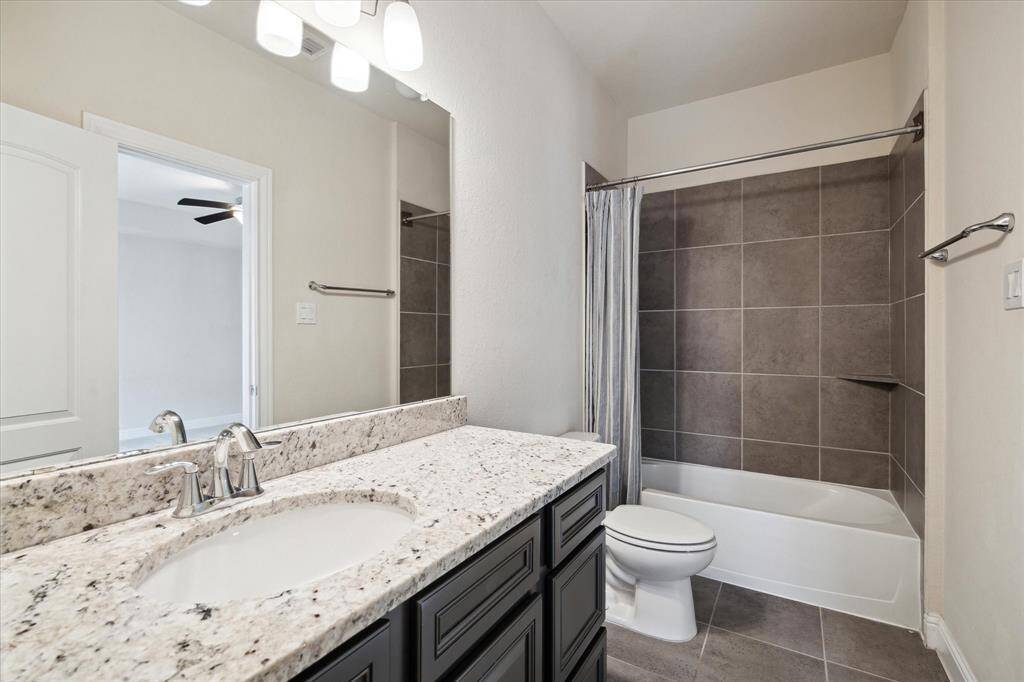 Modern bathroom featuring a granite countertop with a sleek sink, dark cabinetry, and a tiled bathtub/shower combination. Neutral colors create a clean, inviting look.