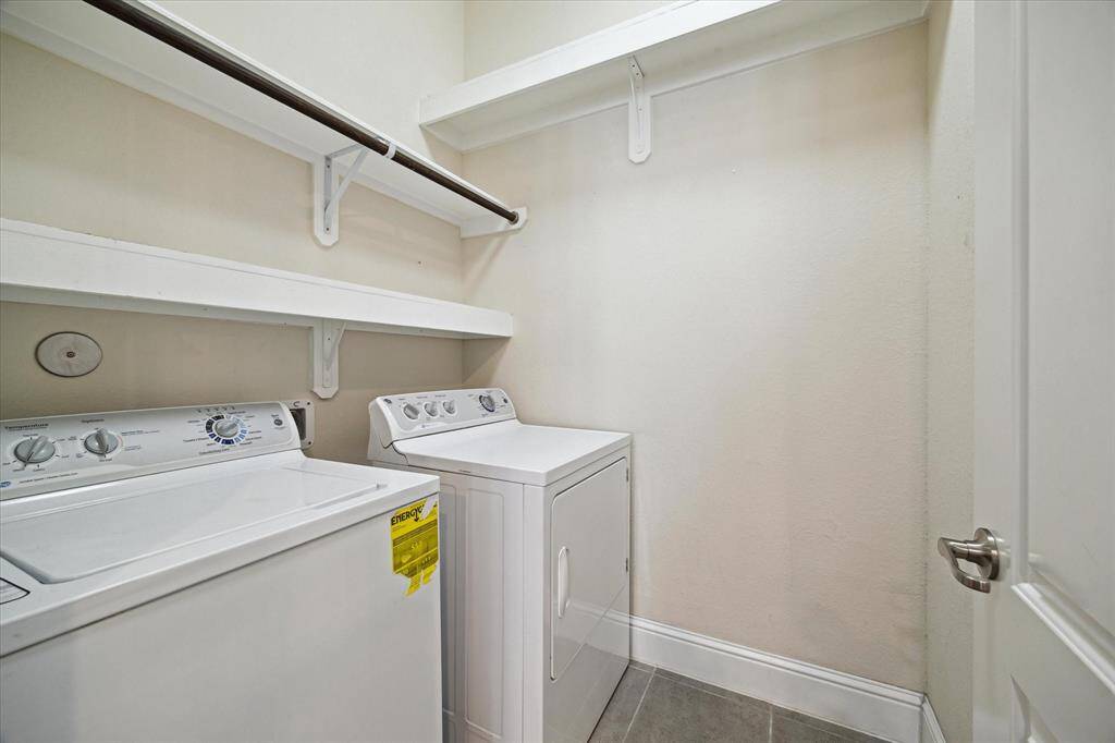 Laundry room featuring a washer and dryer, with upper shelves for storage. The space has neutral walls and a tiled floor, offering functionality and convenience.