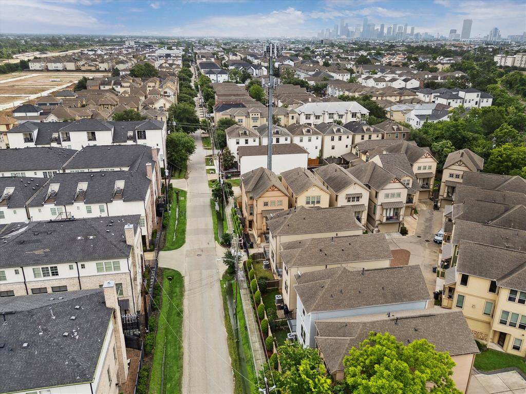This aerial photo showcases a suburban neighborhood with rows of modern townhouses, tree-lined streets, and close proximity to a city skyline, offering a blend of urban convenience and residential charm.