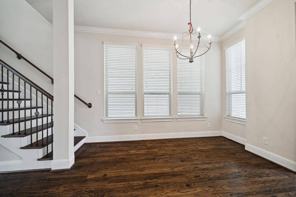 Bright dining area with large windows, elegant chandelier, and hardwood floors. Features a staircase with decorative iron railing, creating a classic and inviting atmosphere.
