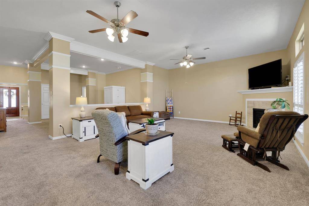 A nice and air living room toward the back of the home featuring a gas log fire place, double ceiling fans, plantation shutters, and crown molding.
