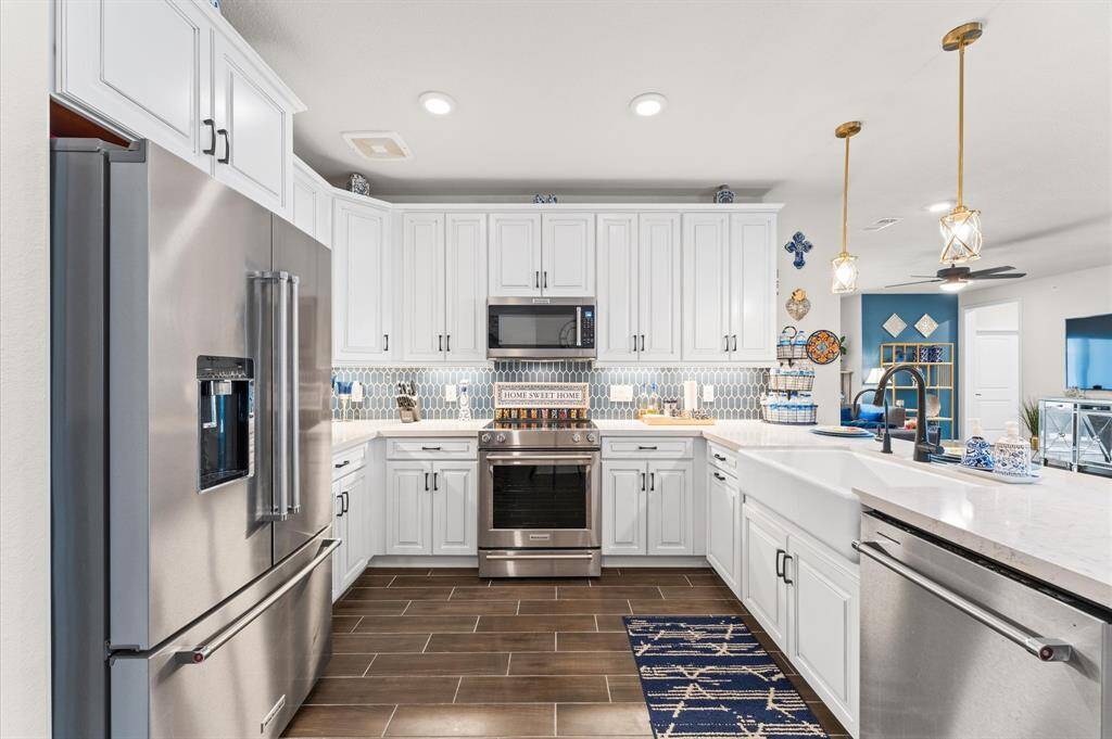The chef’s kitchen boasts white shaker cabinetry, stainless steel appliances, custom backsplash, and quartz countertops.