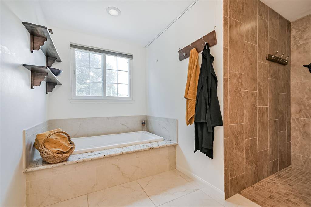 A serene spot to unwind—this large soaking tub features a granite surround, a beautiful window that brings the outdoors in, and thoughtfully placed shelving for extra storage. Pure relaxation, right at home.