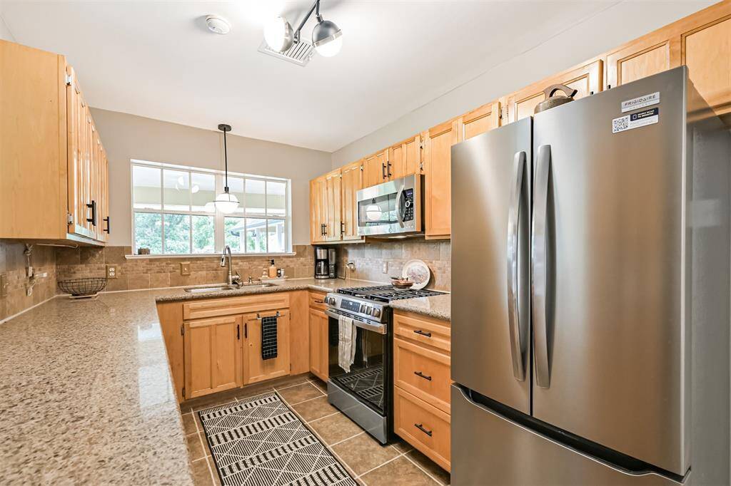 Your first peek at the beautifully updated kitchen—featuring granite countertops, modern light fixtures, and a large undermount sink perfectly placed beneath a window overlooking the backyard.