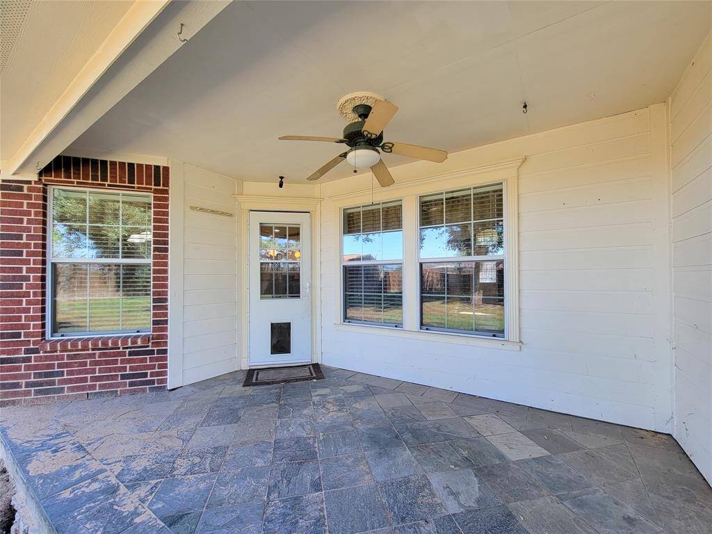 This photo shows a cozy patio area with a ceiling fan, tiled floor, and ample natural light from large windows on interior. It features a mix of brick and siding, providing a charming and inviting space ideal for relaxation or entertaining.