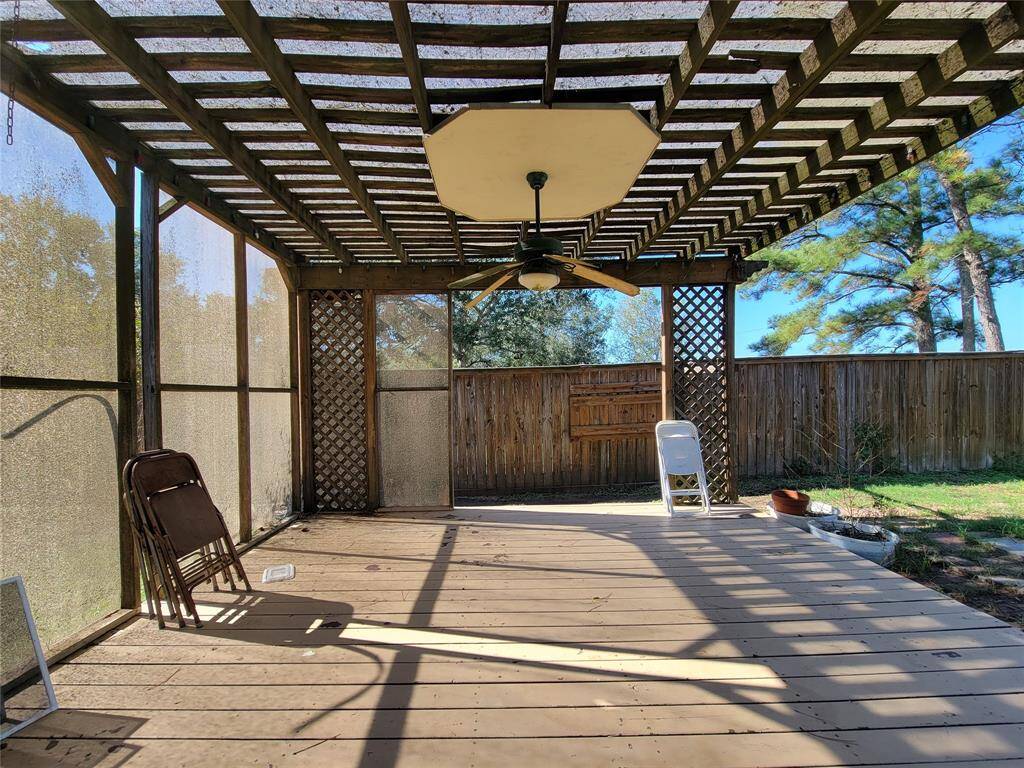 This photo showcases a backyard patio with a wooden pergola, providing partial shade. It features a ceiling fan, lattice accents, and is enclosed by a wooden fence, offering privacy and a cozy outdoor space for relaxation or entertaining.