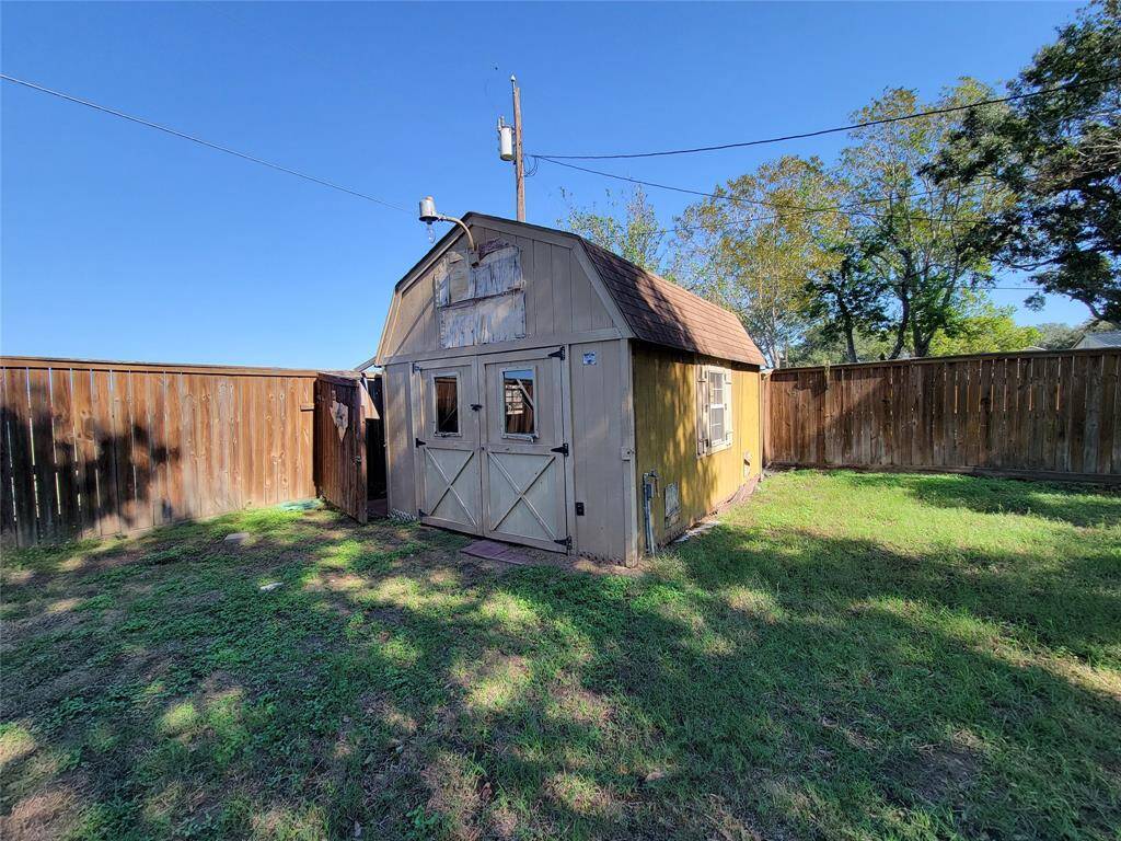 This photo shows a spacious backyard with a wooden storage shed. The area is enclosed by a tall wooden fence, providing privacy. The lawn is grassy with some mature trees in the background, offering a serene outdoor space.