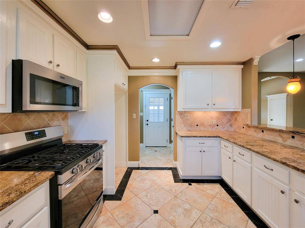 This is a well-maintained kitchen featuring white cabinetry, granite countertops, stainless steel appliances, and tiled flooring. It has a bright, open feel with recessed lighting and a view into the adjacent hallway.