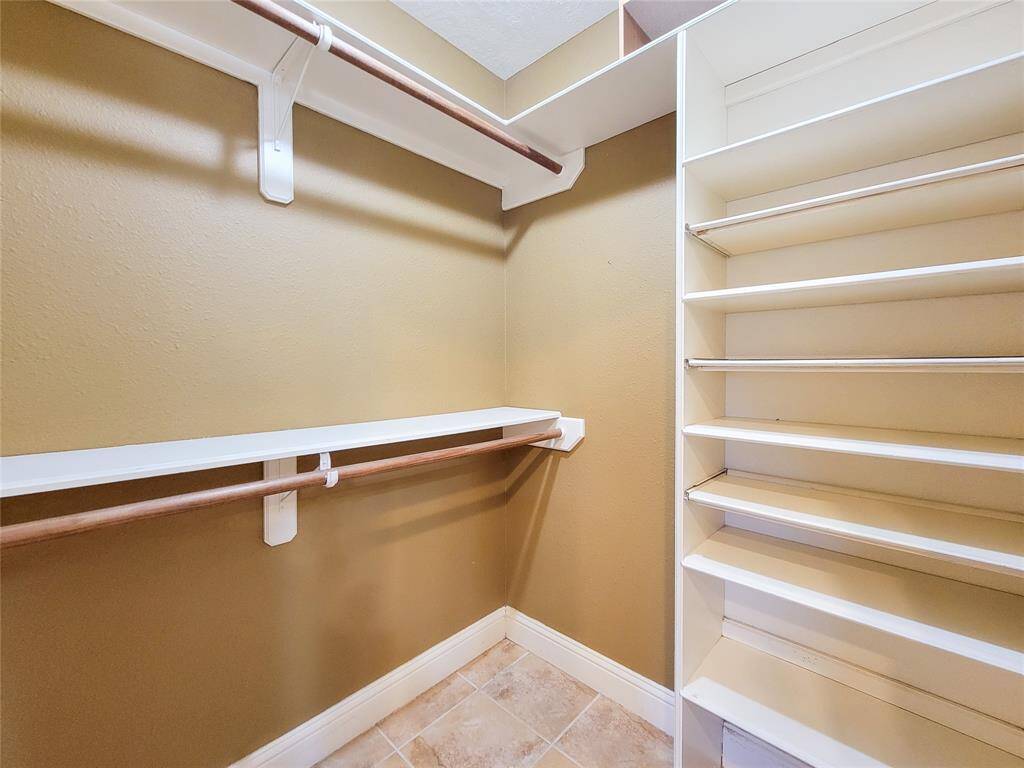 This photo showcases a spacious walk-in closet with ample shelving and hanging rods, perfect for organizing clothes and accessories. The neutral color palette and tiled flooring add a touch of elegance.