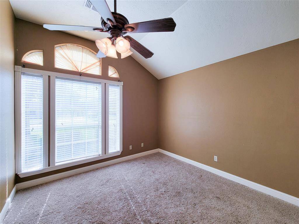 This is a well-lit room featuring a large window with blinds, an arched transom window above, plush carpeting, neutral walls, and a ceiling fan with lights.