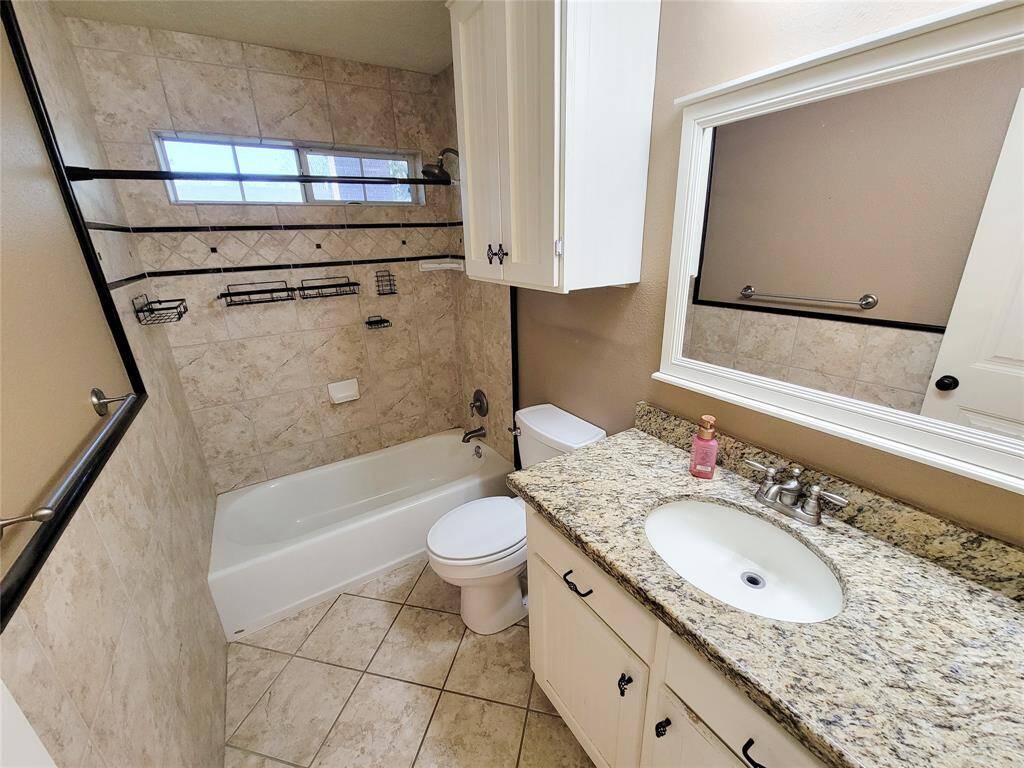 This is a well-maintained bathroom featuring a combination bathtub and shower with tile surround, a single vanity with ample counter space, and under-sink storage. It's brightened by natural light from a frosted glass window.