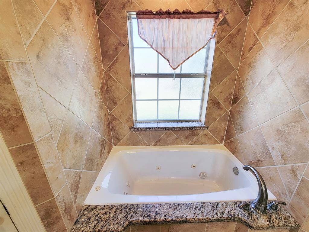 This bathroom features a luxurious jetted bathtub with elegant granite surround and warm tiled walls, complemented by a frosted window that offers natural light and privacy.
