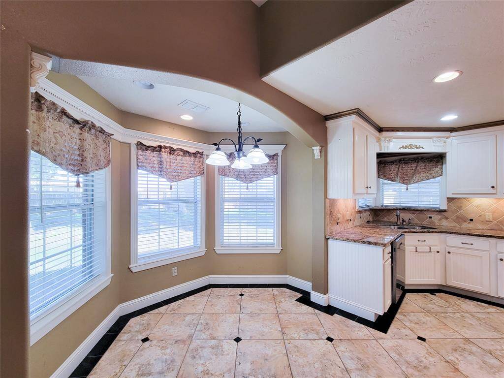 This is a spacious, well-lit kitchen with ample natural light, featuring white cabinetry, granite countertops, and a tiled floor. It includes a cozy breakfast nook with a view from the bay windows, accented with patterned window treatments.