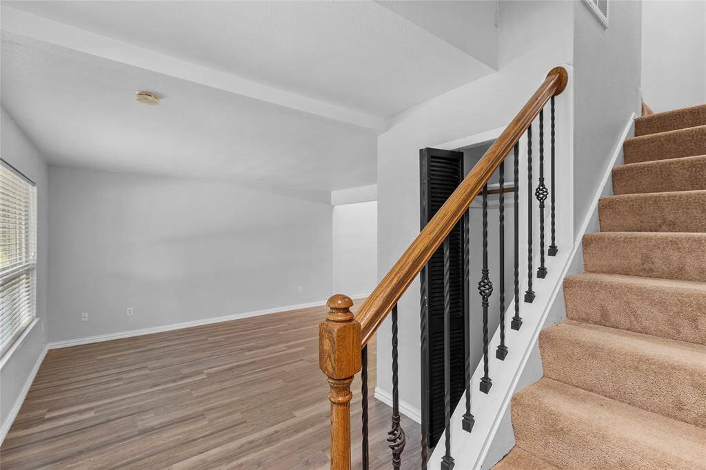 Your bright, open living space is filled with natural light, thanks to large windows that bring the outdoors in. The laminate wood flooring adds warmth, while the staircase with carpeted steps and decorative iron railings leads to your inviting upper level.