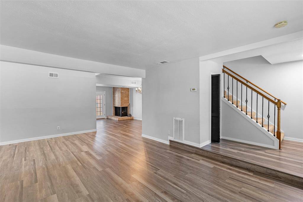 This photo showcases your spacious, open-concept living area with light wood flooring and neutral walls. A cozy fireplace adds warmth in the background, while a staircase with wooden handrails leads to the upper level, combining charm with functionality. This is the photo without virtual staging, giving you a true sense of the room's potential.