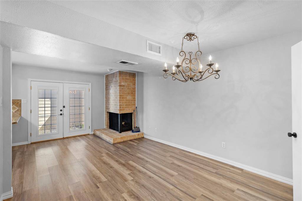 Your dining room features elegant wood flooring, a brick fireplace, and a decorative chandelier. French doors lead outside, filling the space with ample natural light. The cozy yet sophisticated ambiance makes it perfect for dining. This is the photo without virtual staging, giving you a true look at the room's natural charm.