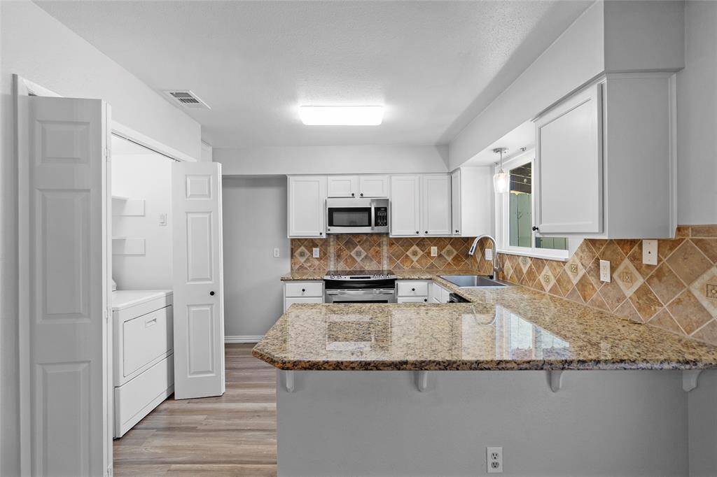 Your bright, open-concept space features a kitchen with granite countertops and stainless steel appliances, adjacent to a living area with modern laminate flooring. A large window fills the space with natural light, creating a warm and welcoming atmosphere.