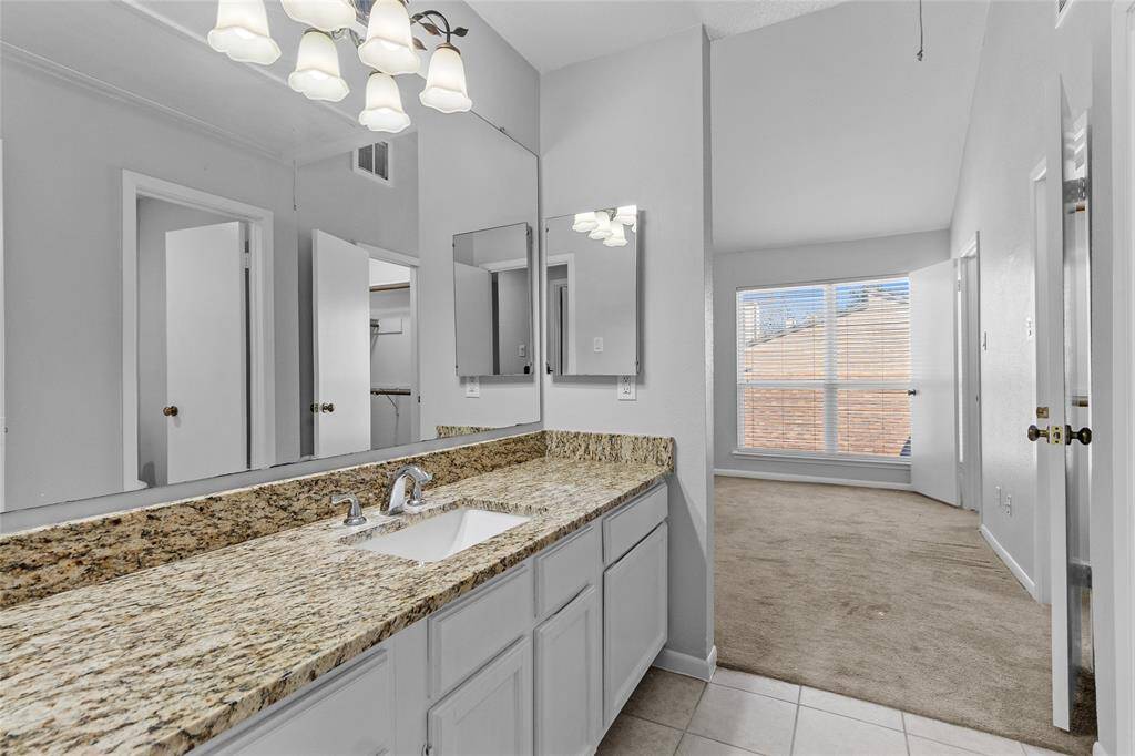 This photo showcases your bright primary bathroom, featuring a granite countertop and single sink. Connected to the primary bedroom, it offers a seamless flow with a carpeted room and large window that fills the space with natural light. Neutral colors and modern lighting create a welcoming and serene atmosphere.