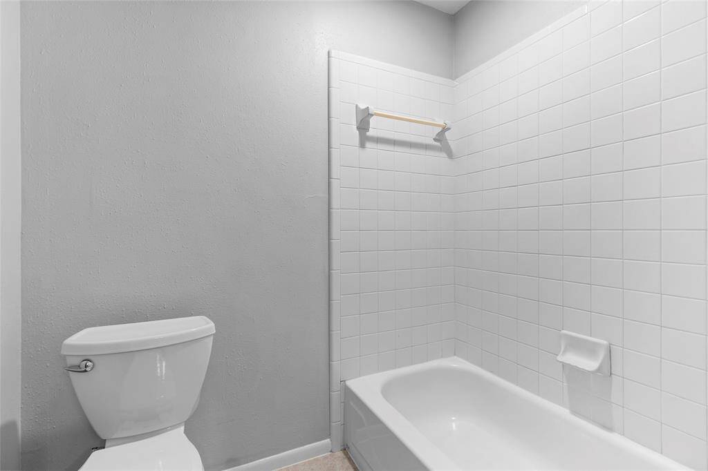 This photo shows a simple, clean space inside your primary bathroom, featuring a white tile shower and bathtub, complemented by gray walls and a standard white toilet. The minimalist design keeps the area functional and easy to maintain.