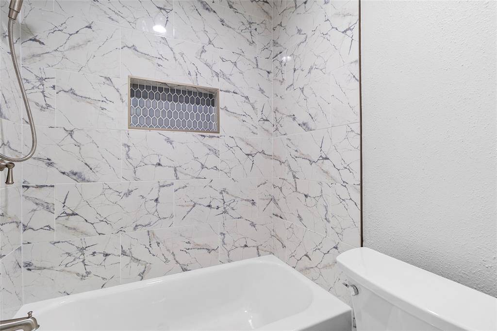 Your secondary bathroom upstairs features elegant marble-patterned tiles with a modern niche for storage, a sleek tub, and a contemporary shower fixture, creating a luxurious and functional design that enhances the space’s beauty and practicality.