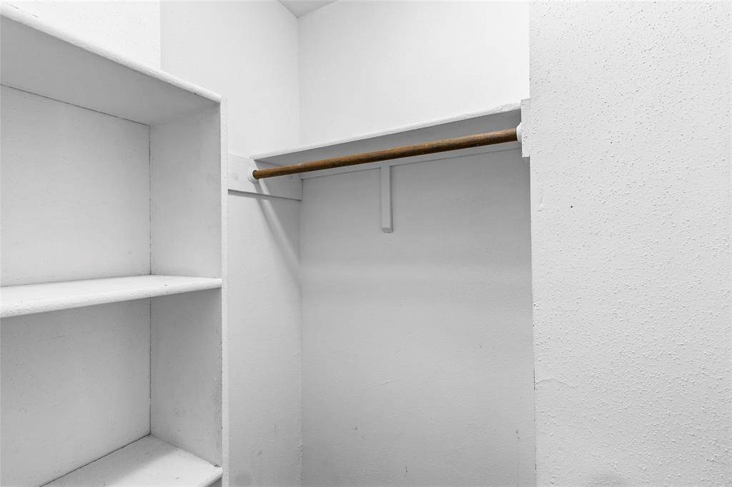 This photo shows your secondary bedroom walk-in closet featuring built-in shelves on the left and a hanging rod for clothes. The clean design makes it a functional and organized area for storage.