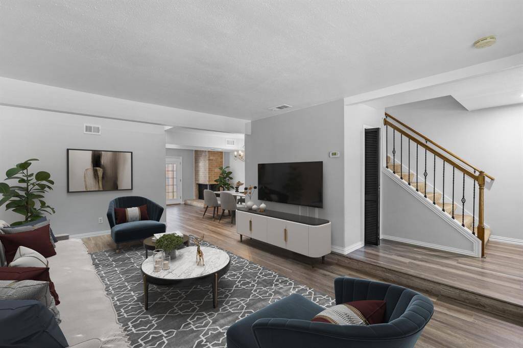 Your modern living room boasts an open and airy design, with neutral walls and warm laminate flooring creating a cozy yet contemporary feel. Glass doors invite natural light to fill the space, while a staircase with wooden railings adds character. The seamless flow into the dining area enhances your home's inviting and connected layout.